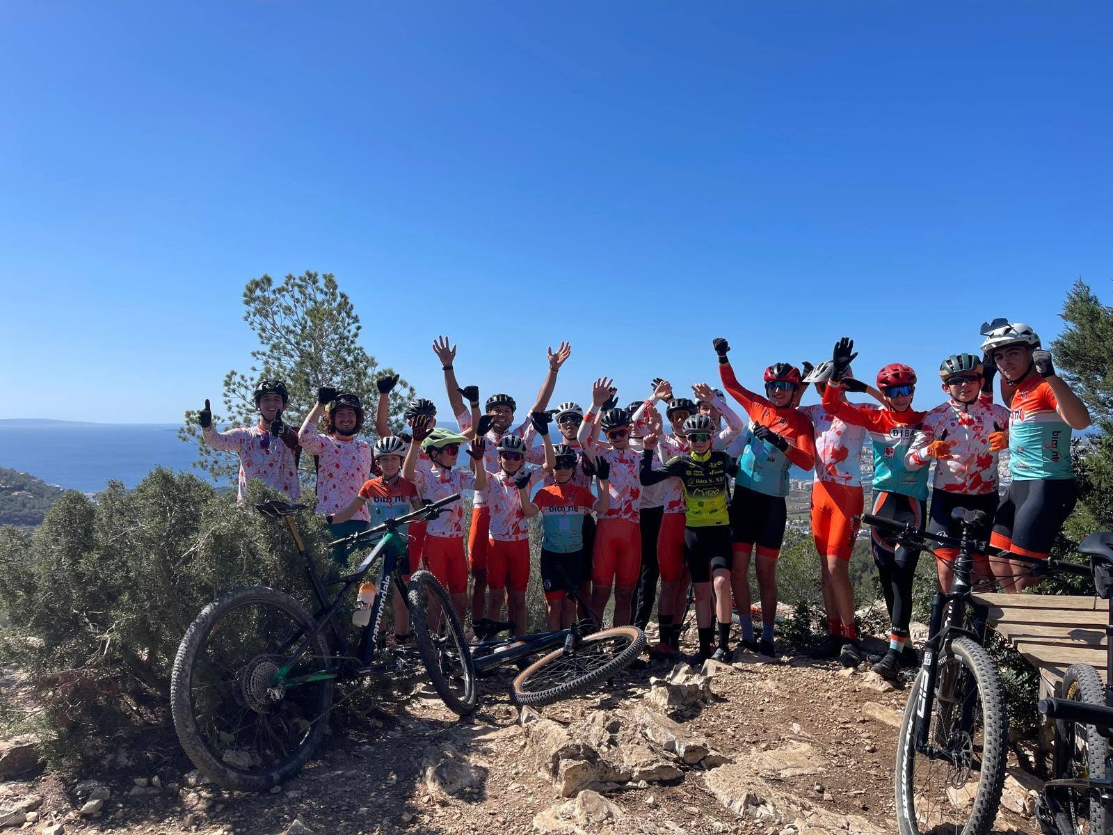 Grup de ciclistes de l'escola Bimont Jove celebrant amb els braços amunt en un mirador amb vistes a la mar